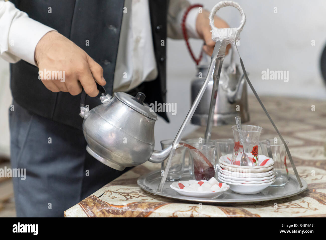 Hands of man (tea maker) with metal Turkish teapot pouring tea into glass cups in a coffee house in Turkey Stock Photo