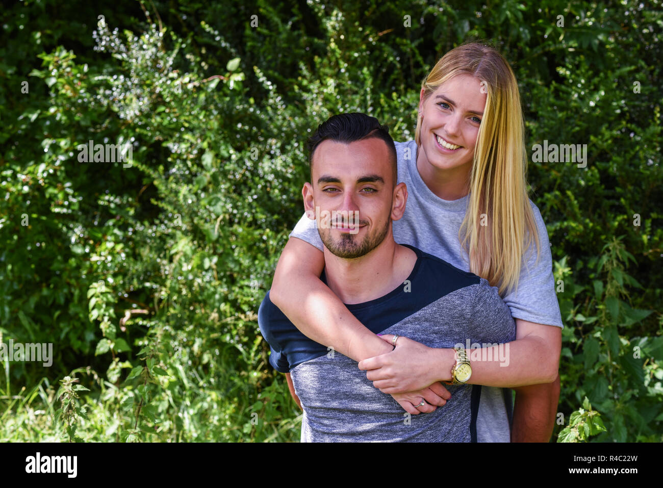 Smiling blonde woman hugging boyfriend from behind Stock Photo - Alamy