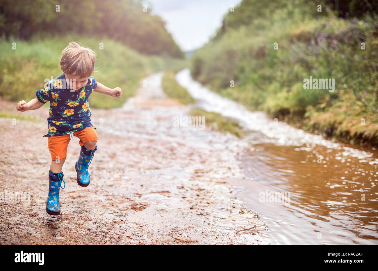 Boy with rubber boots enjoys rainy day in rural surrounding Stock Photo