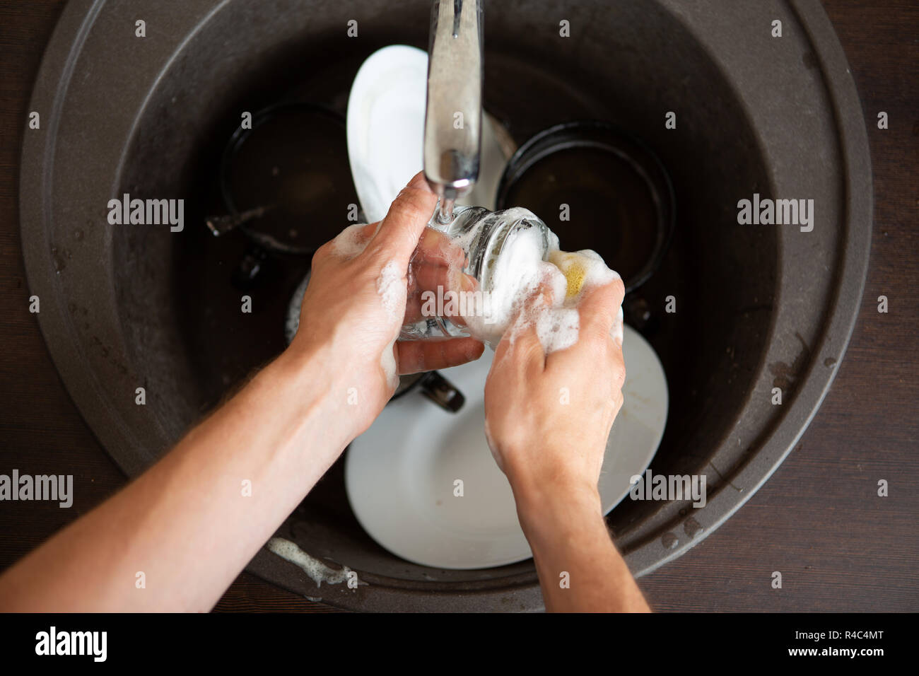 Picture from above of man's hands washing dish into sink Stock Photo