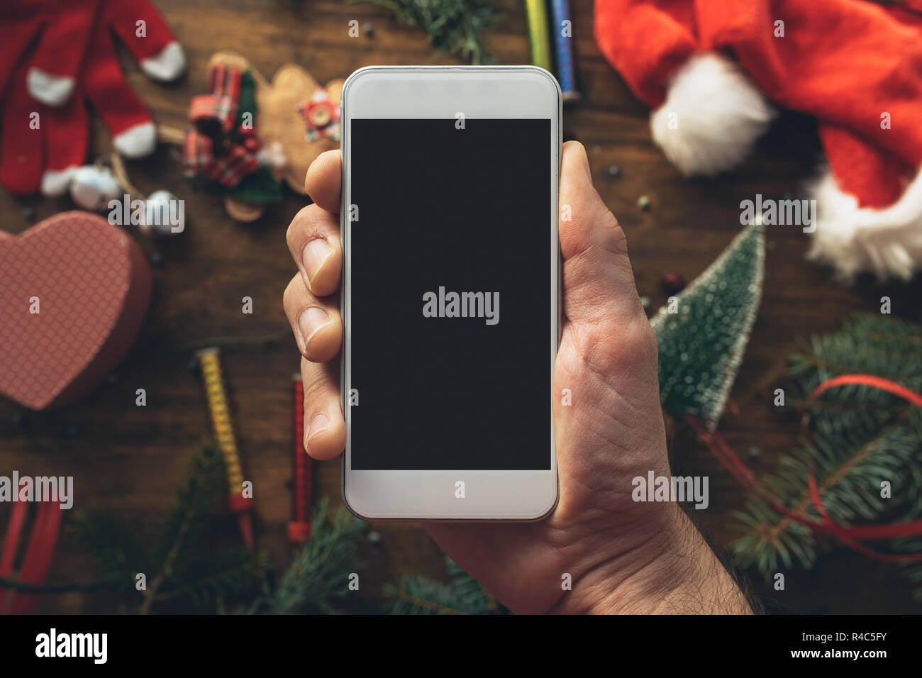 Smartphone in hand for Christmas season mock up with festive holiday decoration in background. Stock Photo