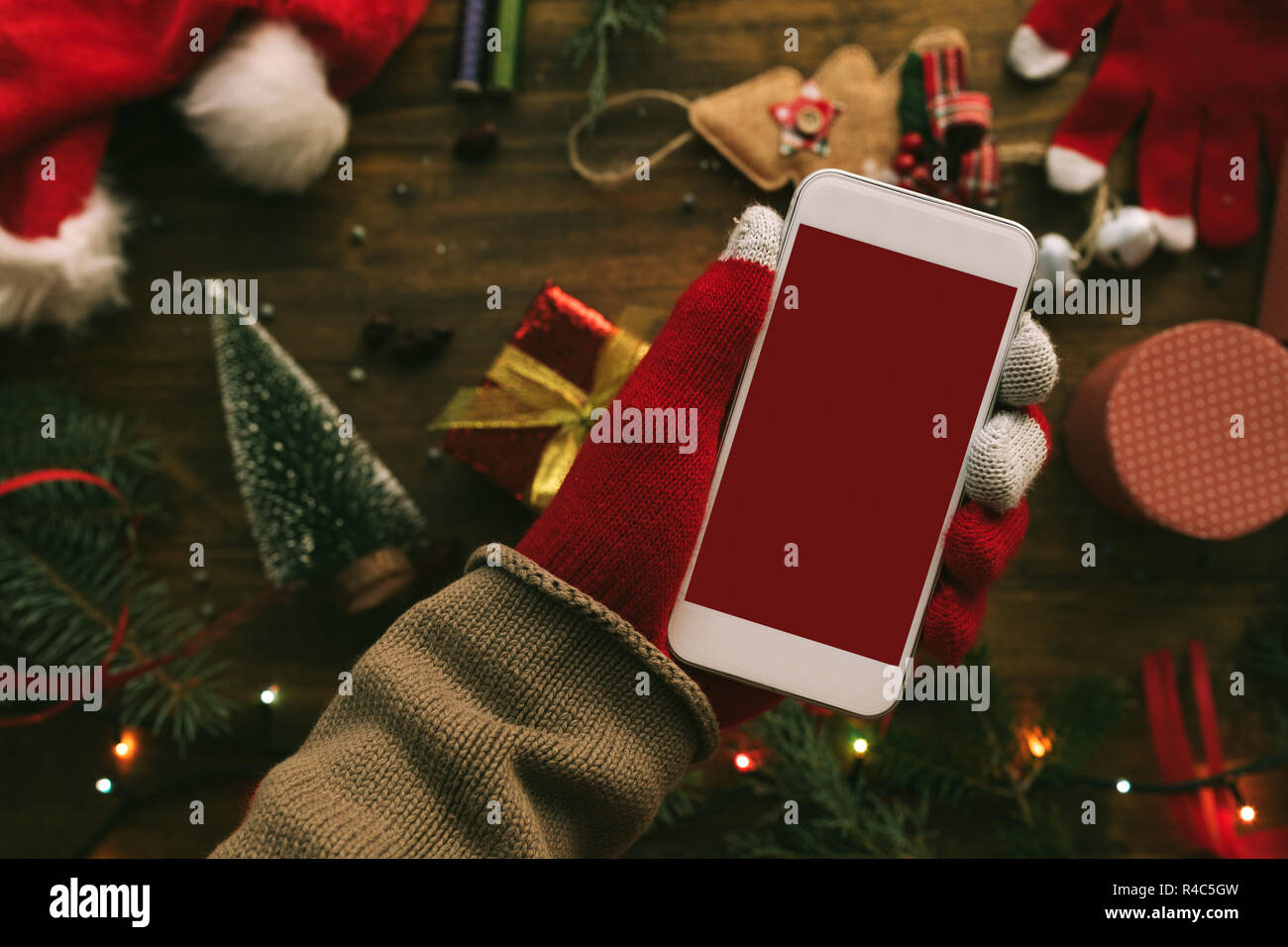 Smartphone in hand for Christmas season mock up with festive holiday decoration in background. Stock Photo