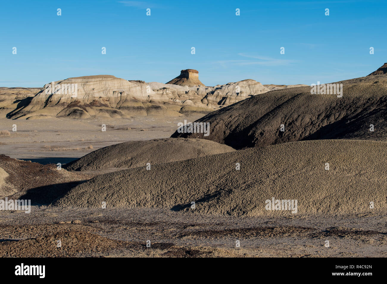 A distant mesa rises above a desert landscape with textured, grainy hills and soil in the Bisti Badlands of New Mexico Stock Photo