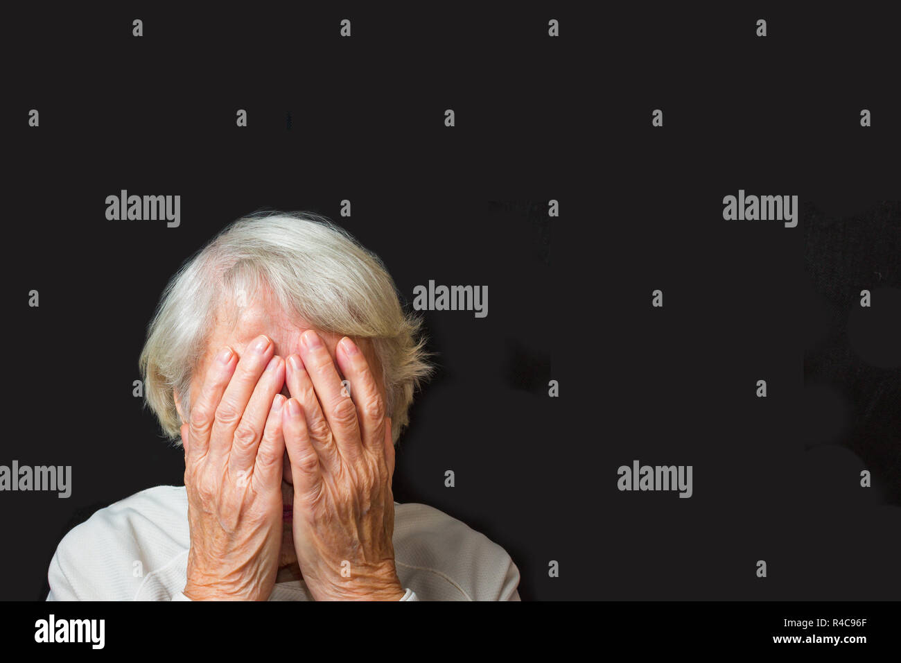 Portrait of an elderly woman with face closed by hands on black Stock Photo