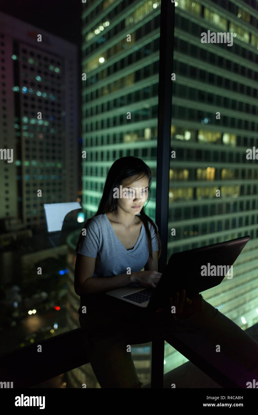 Young beautiful Asian woman using laptop against glass window wi Stock Photo