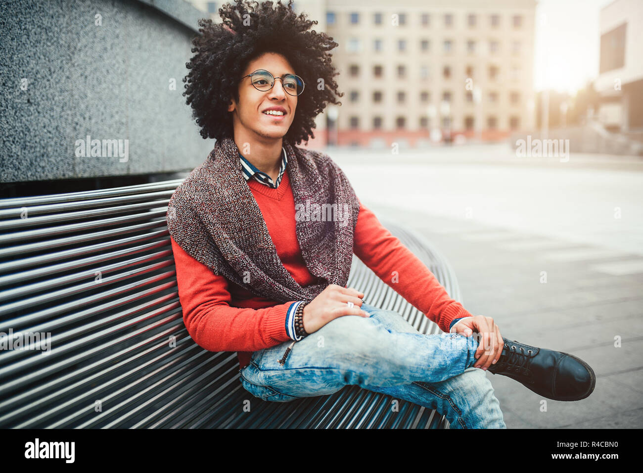 A handsome young Egyptian curly guy sitting on a bench dressed in a bright  orange sweater and jeans. Happy people. The student walks in the break betw  Stock Photo - Alamy, image size:1300x956