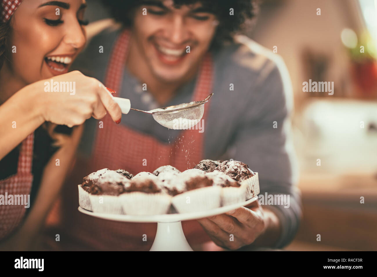 Happy loving couple is sprinkling powdered sugar on roasted chocolade muffin. Stock Photo