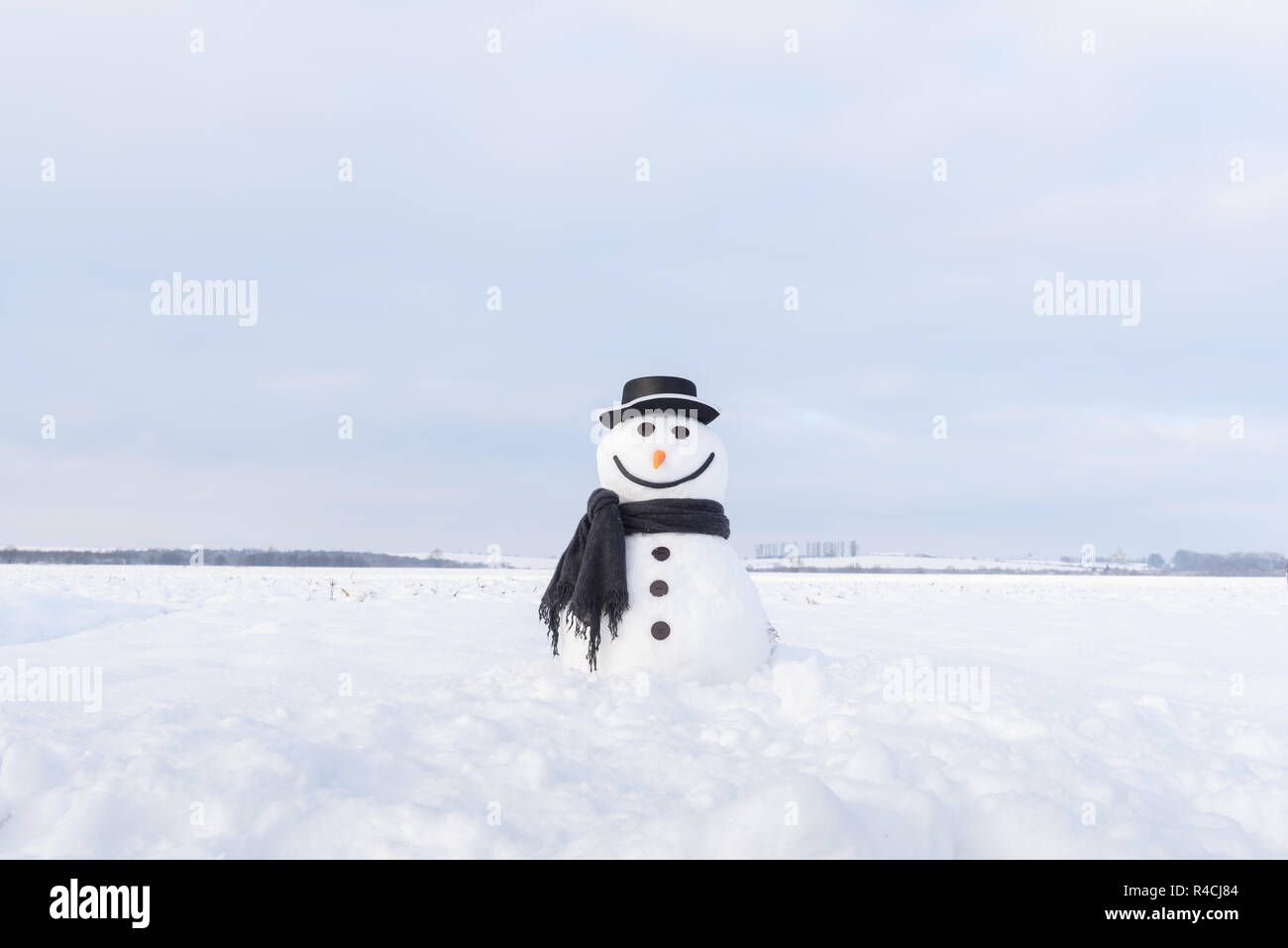Funny snowman in stylish hat and black scalf on snowy field Stock Photo