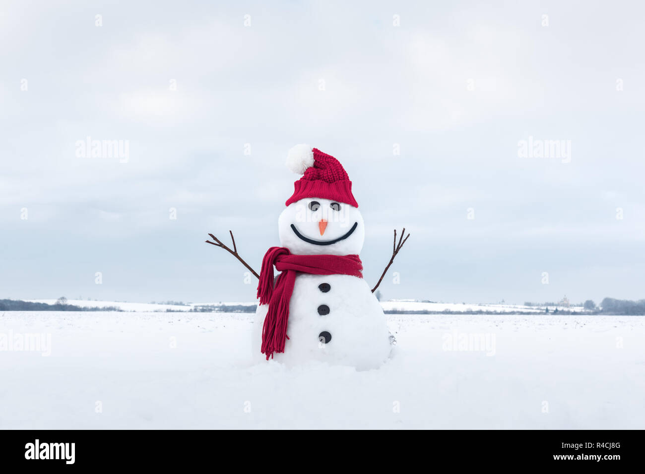 Funny snowman in stylish santa hat and red scalf on snowy field Stock Photo