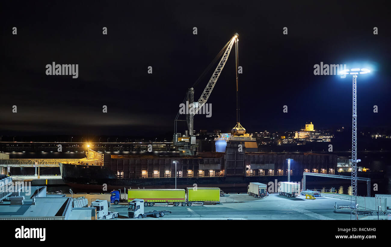 mechanical hydraulic clamshell grabbers loading coal on ship at night. Stock Photo
