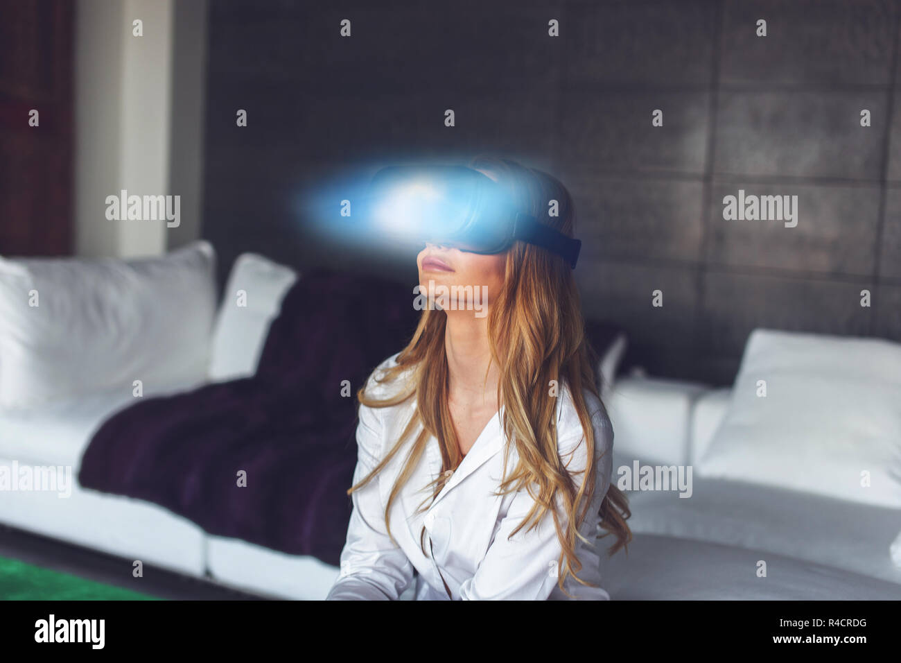 Young blonde woman with VR headset and magical blue light light at home concept, virtual reality Stock Photo