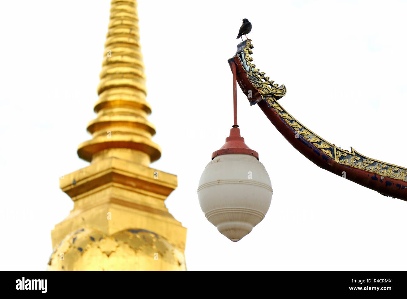 Thai Vintage Boat Shaped Street Lamp with a Black Bird Perching on the Top and Golden Chedi in Background, Historic Place in Nan Province, Thailand Stock Photo