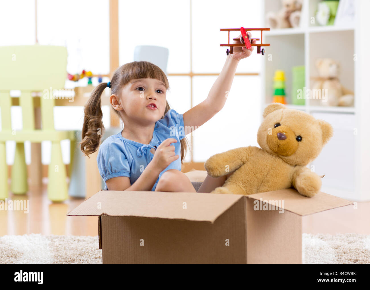 Child girl playing pilot flying a cardboard box in nursery room Stock Photo