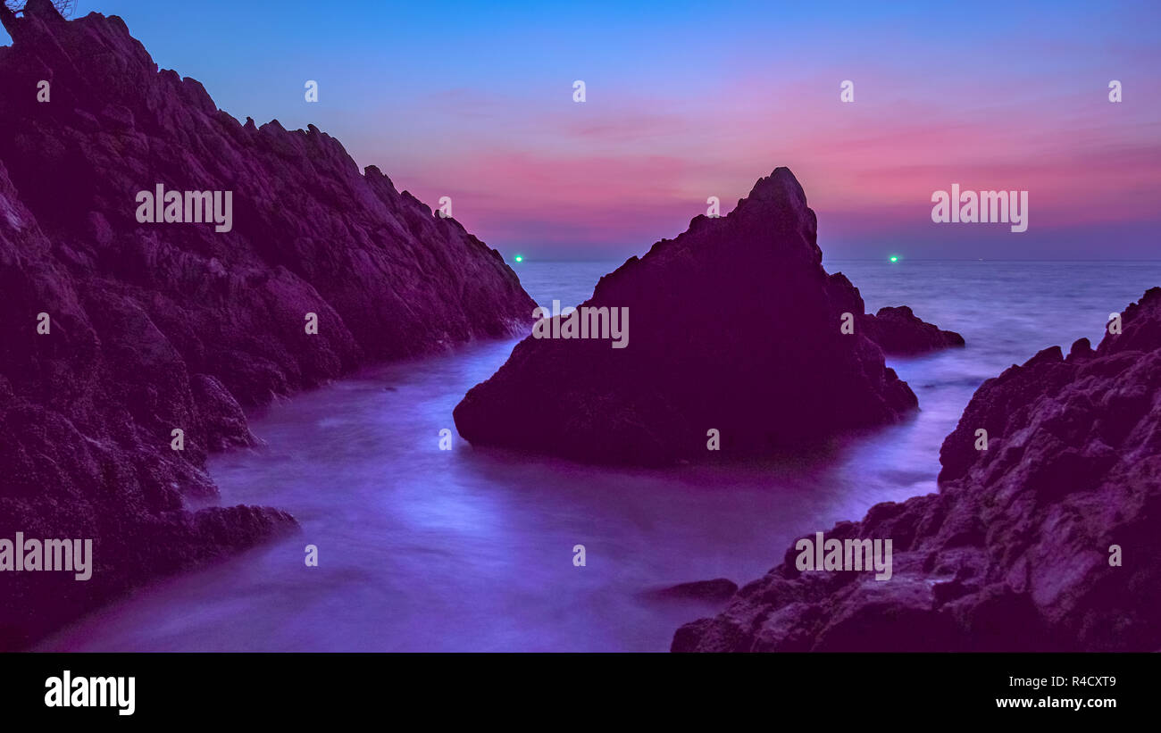 waves hit the big cone shape rock in the middle of stone cape during sunset at banana beach Phuket Stock Photo