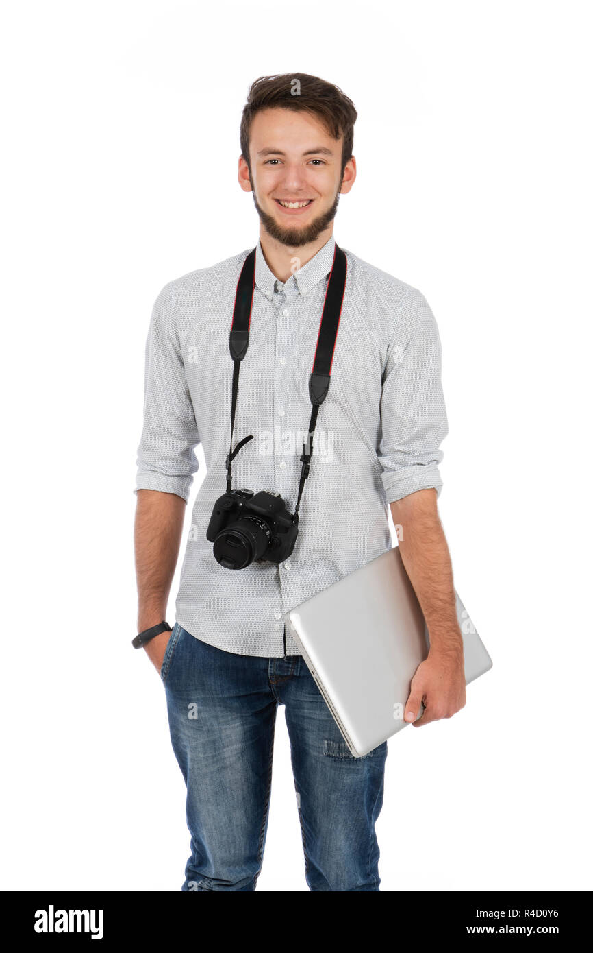 Nerd boy with camera around his neck and computer under his arm, he is standing in the studio and is wearing casual clothes Stock Photo