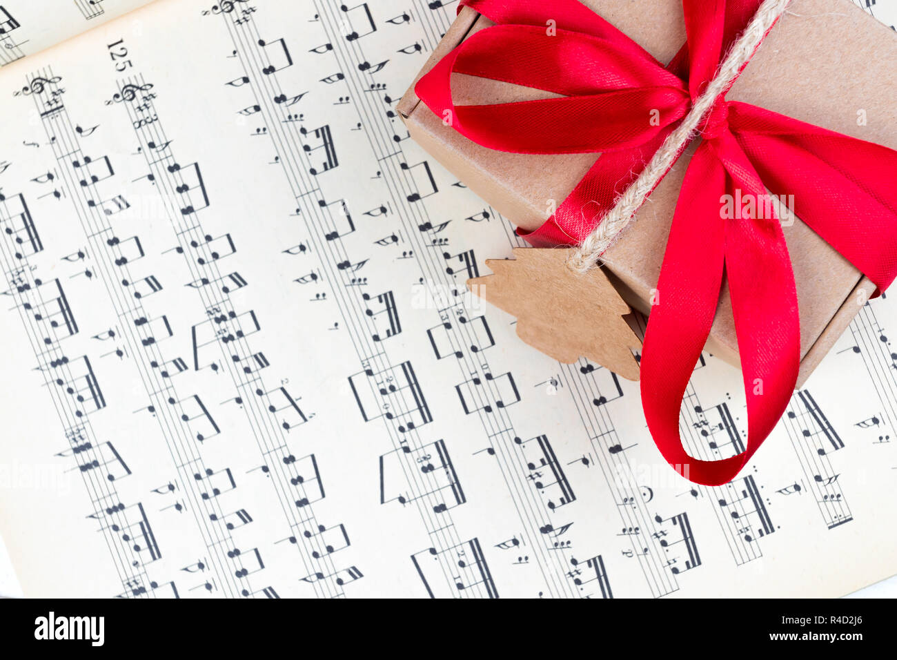 Christmas gift or present with label and twine on music sheet. Red ribbon bow. Notes. Overhead