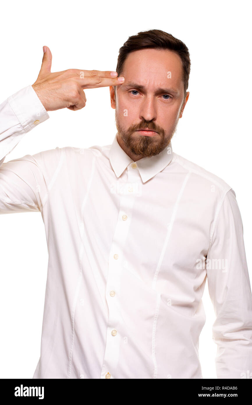 Young man committing suicide with finger gun gesture, shooting himself in head making finger pistol sign, man in white shirt on white background, copy space Stock Photo