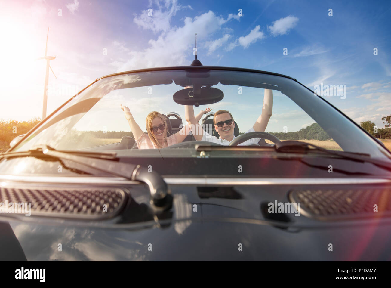 young couple in cabriolet raises their arms high with happiness Stock Photo