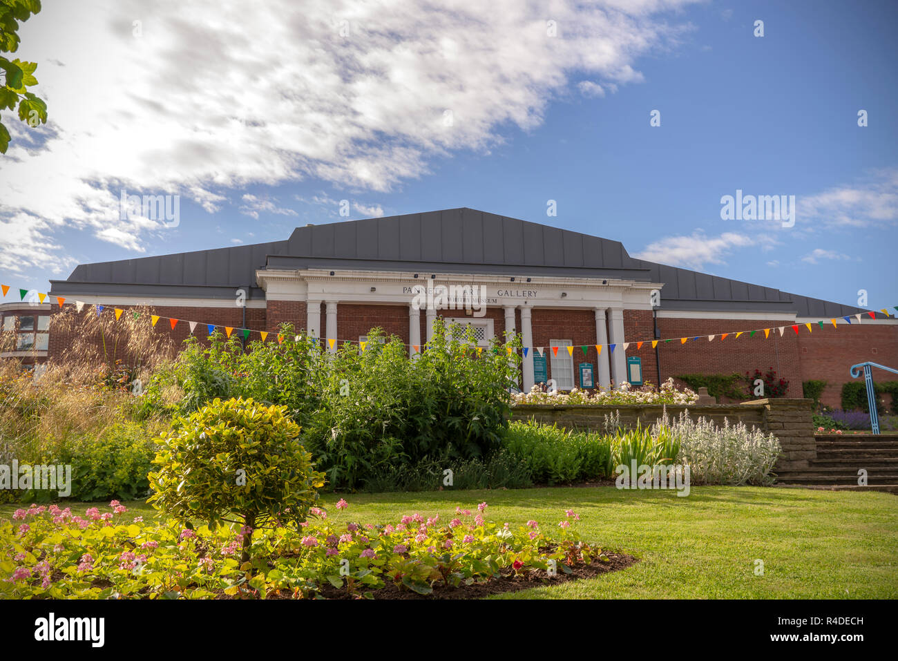 Art Gallery building set in a park,  A neat lawn with a flower bed is in the foreground and a blue sky with clouds are above. Stock Photo