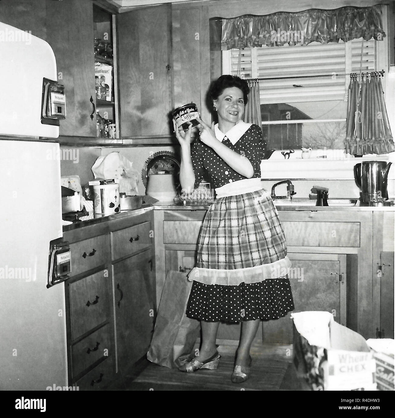 Young suburban housewife in her kitchen holding up a can of coffee, circa 1950s, USA. Stock Photo