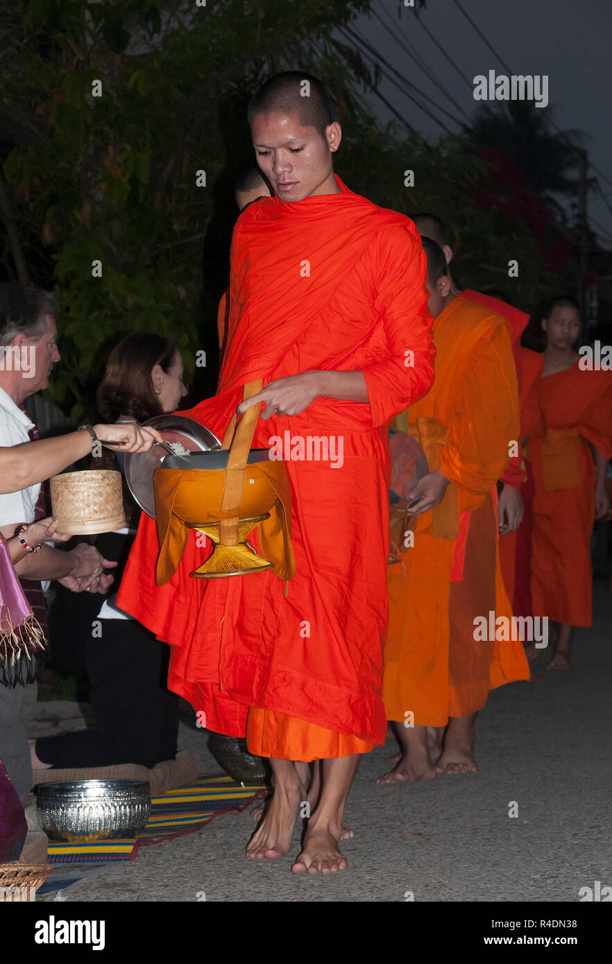 Starting before daybreak orange-robed Laos Buddhist monks take alms from the devoted every day in early morning - Luang Prabang, Northern  Laos. Stock Photo
