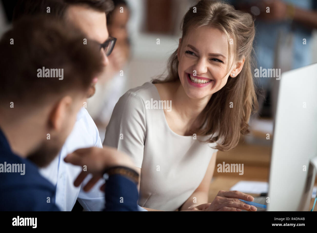 Smiling young woman talking with colleagues at shared workplace Stock Photo