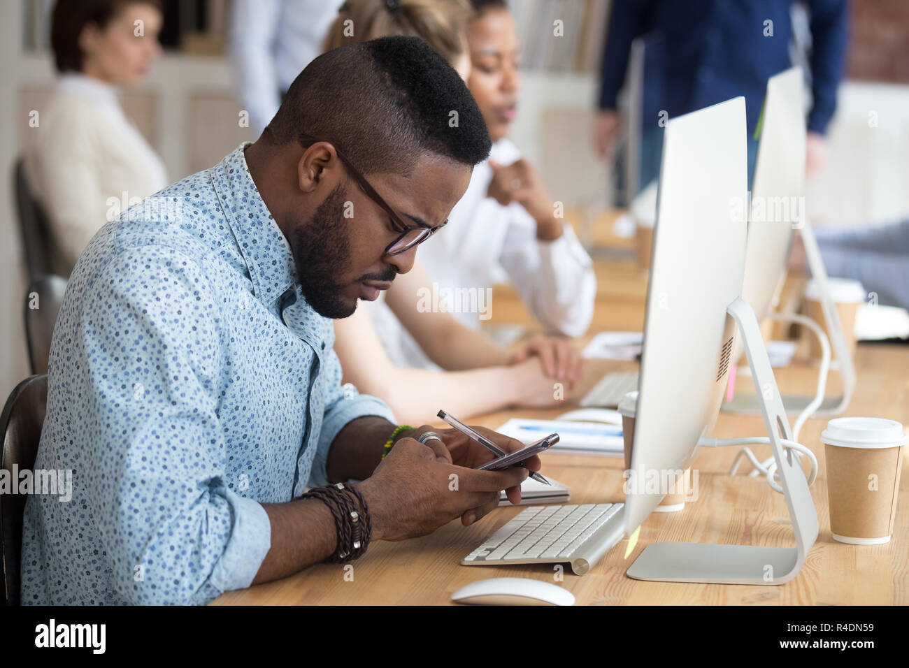 Serious African American man using smartphone at workplace Stock Photo