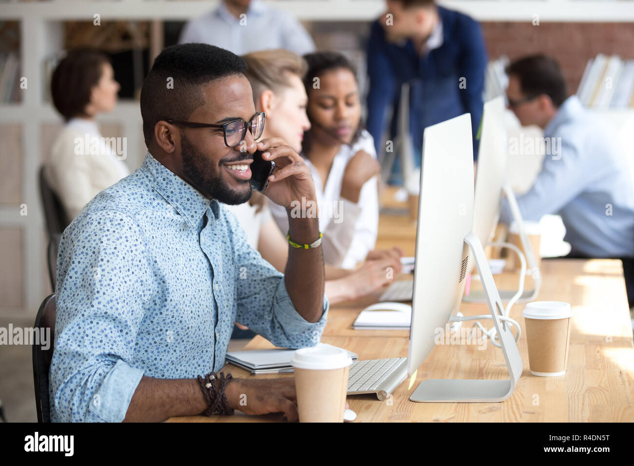 Smiling African American man talking by phone, using computer Stock Photo