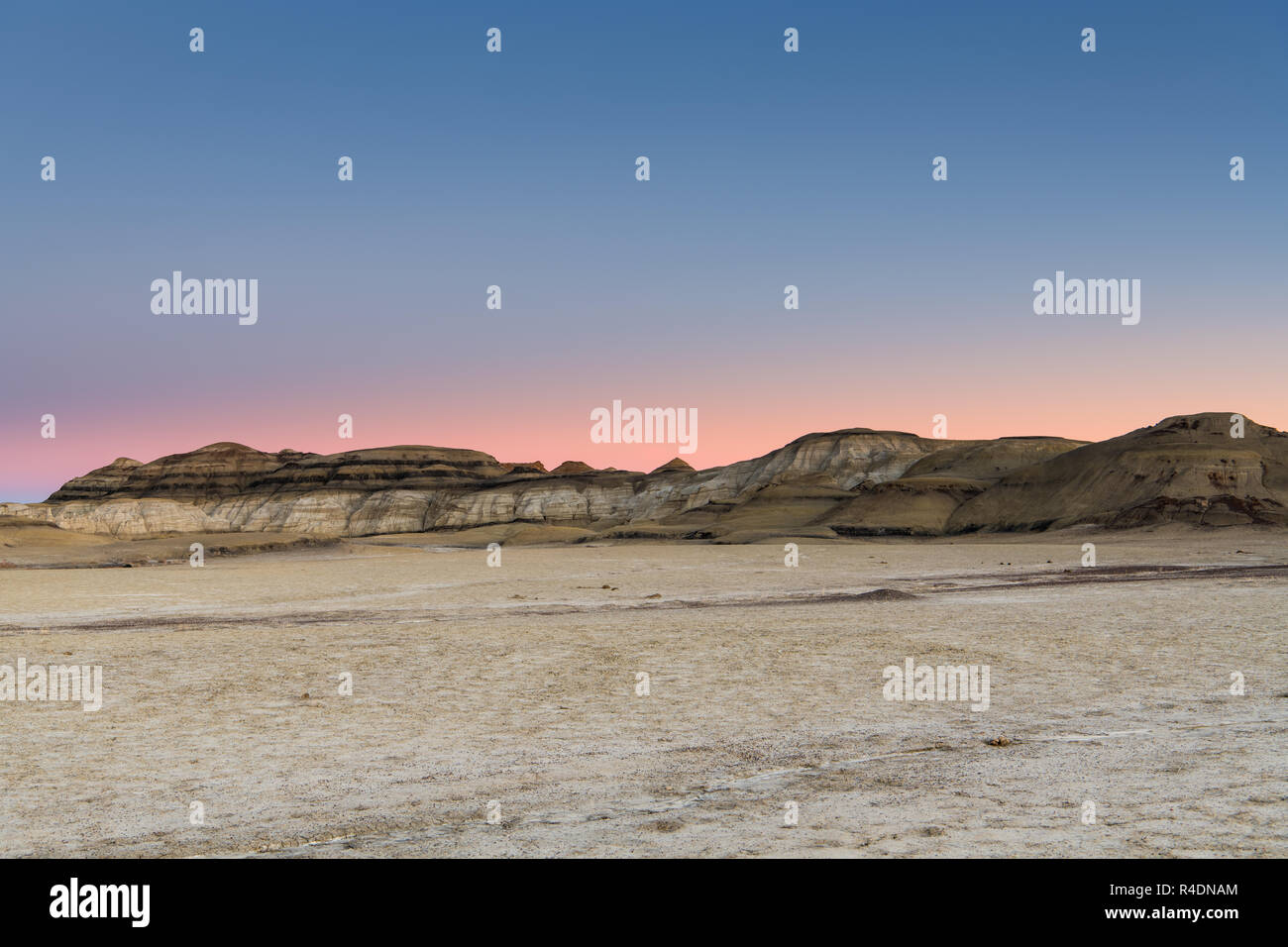 The desert landscape and hills of the Bisti Badlands of New Mexico at sunset under a beautiful sky with pink, peach, purple, and blue hues Stock Photo