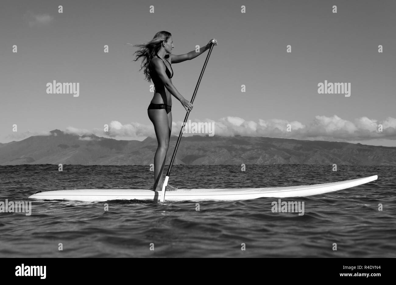 Fit, athletic woman stand up paddles at Napili Bay, Maui, Hawaii with Molokai in the distance. Stock Photo