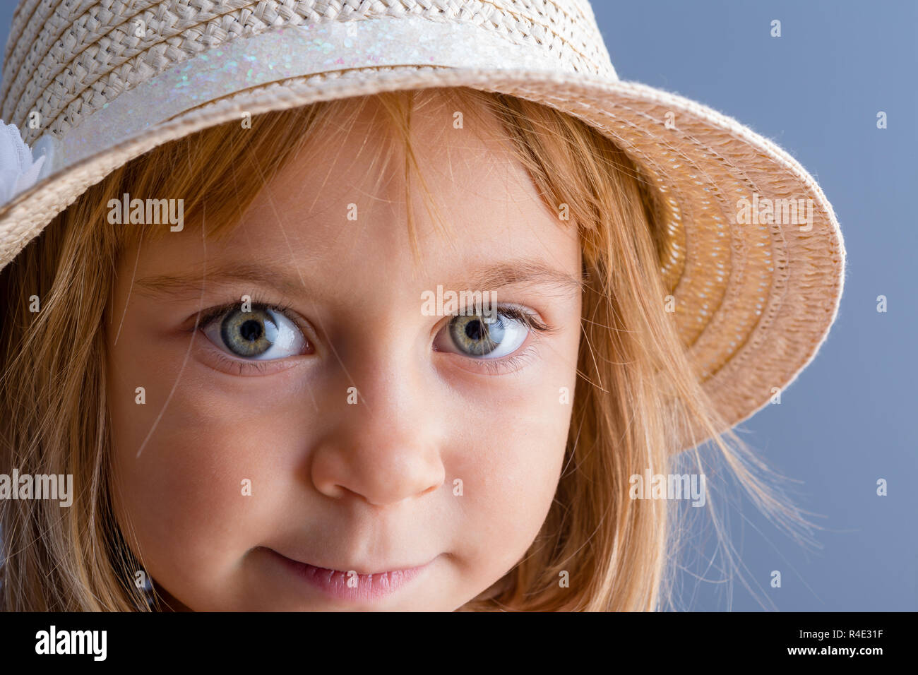 Pretty little girl with large green eyes wearing a trendy straw hat looking at the camera with a quiet smile Stock Photo
