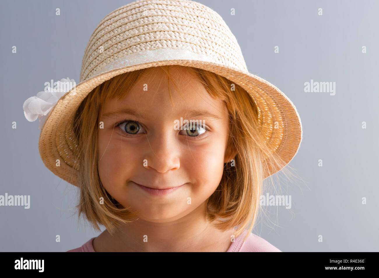 Adorable little four year old blond girl with huge green eyes smiling happily at the camera wearing a trendy straw hat Stock Photo