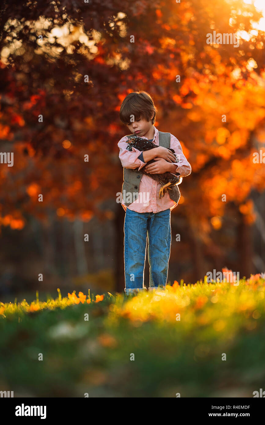 Boy standing outdoors cuddling a chicken, United States Stock Photo