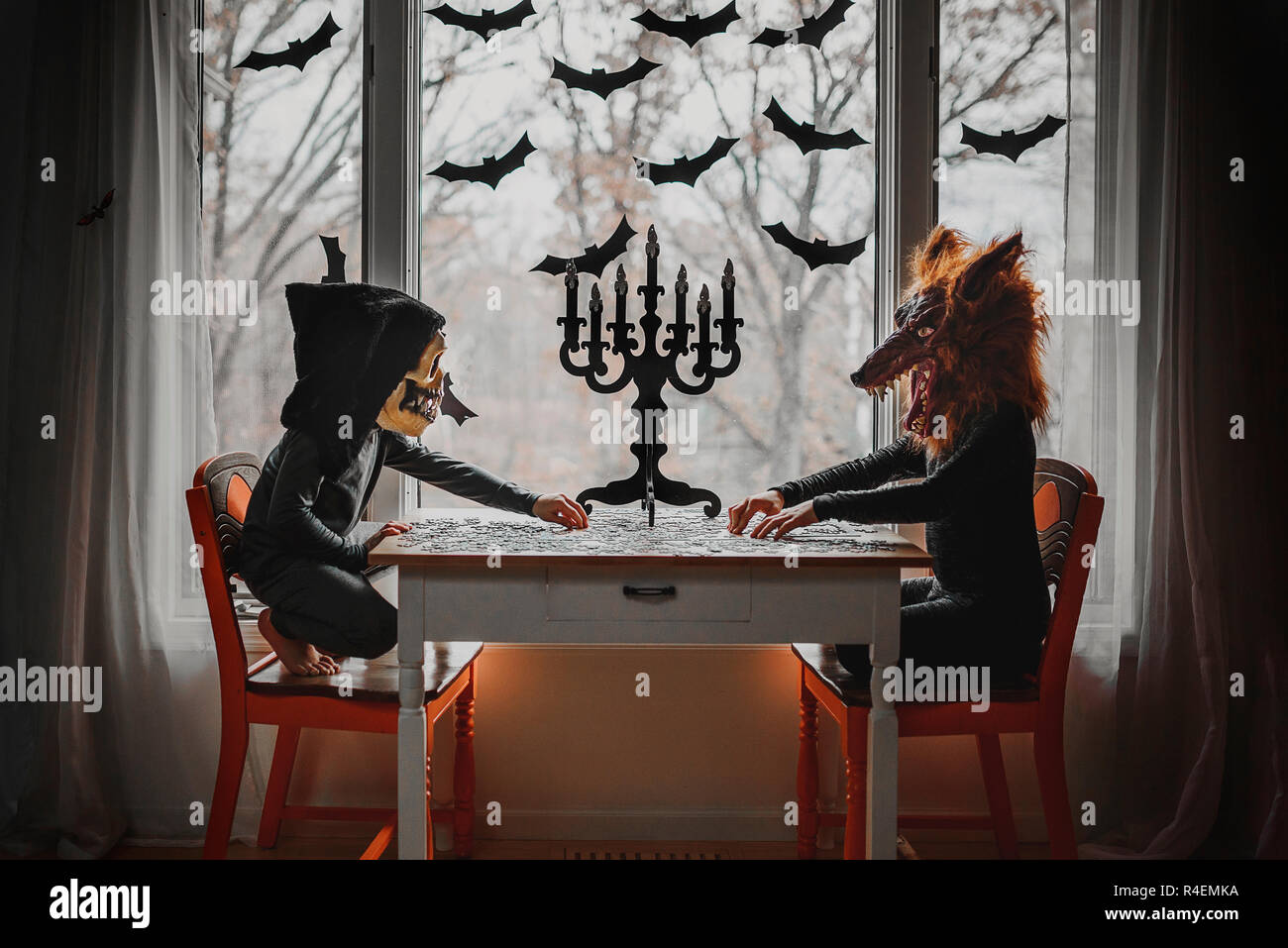 Two children in Halloween costumes sitting by a window doing a puzzle, United States Stock Photo