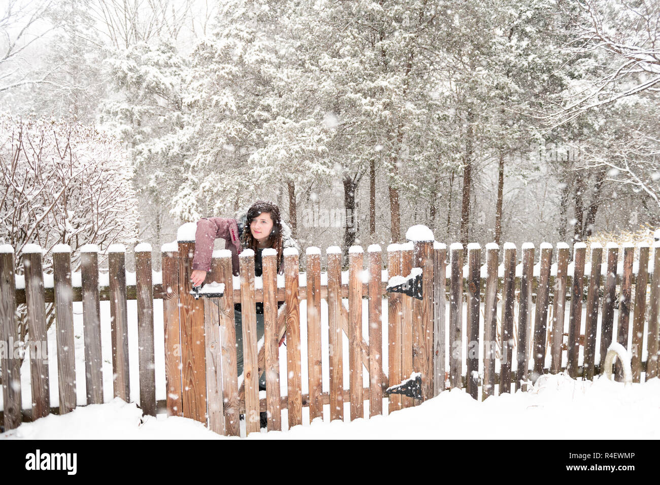 Young woman standing, opening wooden home, house fence gate outside, outdoors, outdoor front yard, backyard, heavy snowstorm, storm, snowing, falling  Stock Photo