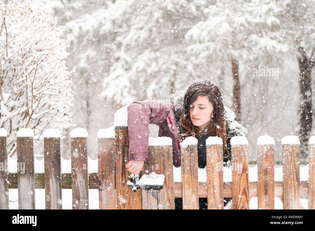 Young woman closeup standing, opening wooden home, house fence gate outside, outdoor front yard, backyard, heavy snowstorm, storm, snowing, falling sn Stock Photo