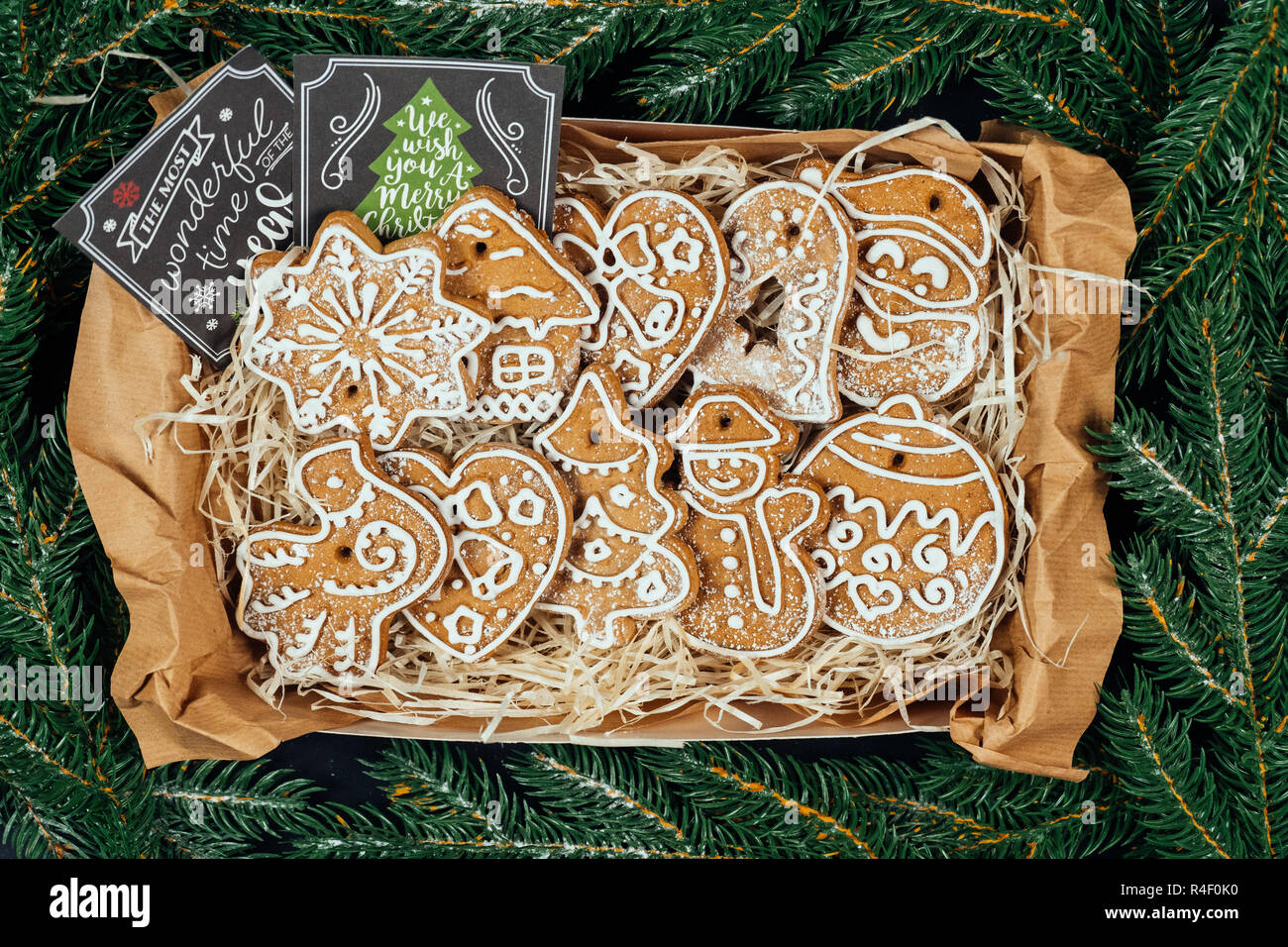 Present box with Christmas gingerbread cookies with glaze and gift cards with Christmas greetings surrounded with green fir branches. Flat lay. Top vi Stock Photo