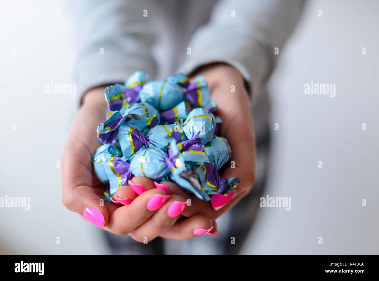 Selective focus-Girl with pink nail varnish holds wrapped chocolate sweets Stock Photo