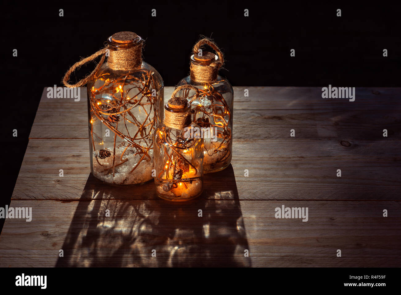 Bottles filled with lights, branches and snow standing on Outdoor Wooden Table Top at night Stock Photo