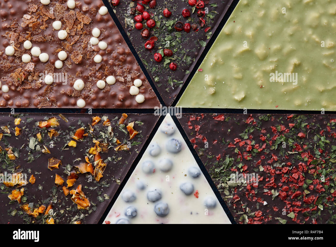 Triangle shaped pieces of handmade chocolate with diverse kinds of toppings, close up view Stock Photo