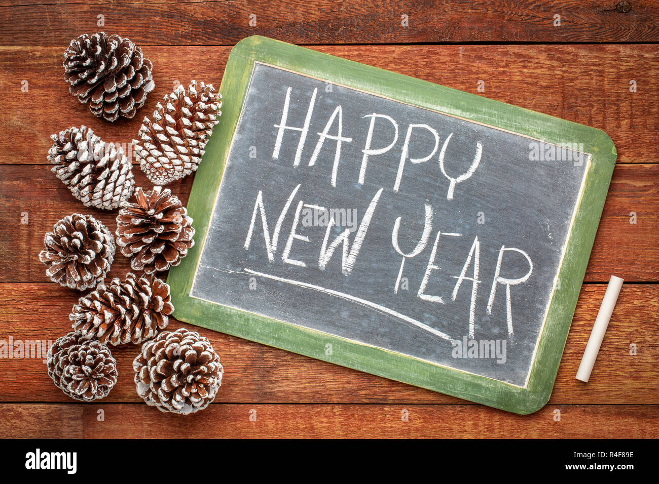 happy new year - white chalk handwriting on a slate blackboard with frosty pine cones against rustic barn wood Stock Photo