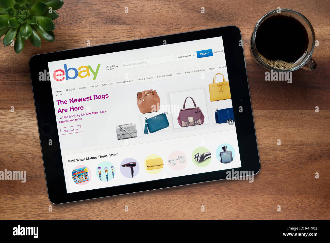 The website of ebay is seen on an iPad tablet, on a wooden table along with an espresso coffee and a house plant (Editorial use only). Stock Photo