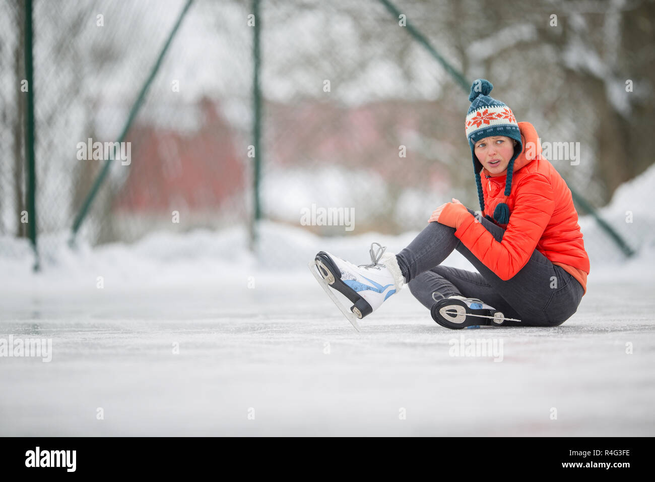 Ice skating concept young woman sitting on the ice rink after falling