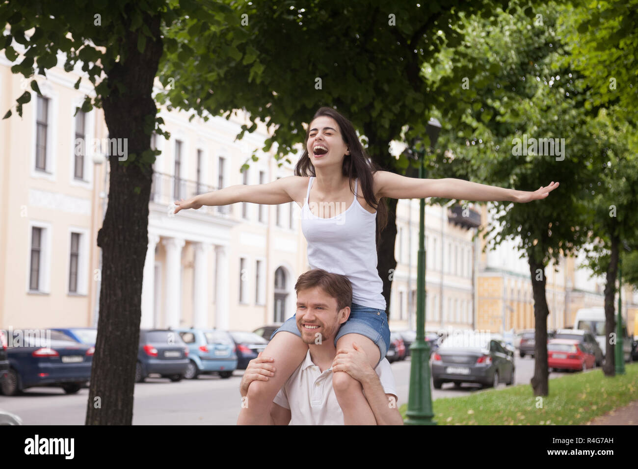 Happy laughing girlfriend sitting on boyfriend shoulders outdoor Stock Photo