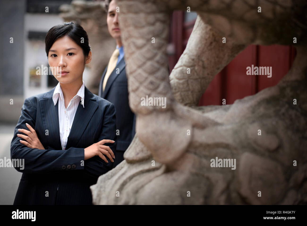 Portrait of a young businesswoman standing with her arms crossed in front of a male colleague. Stock Photo