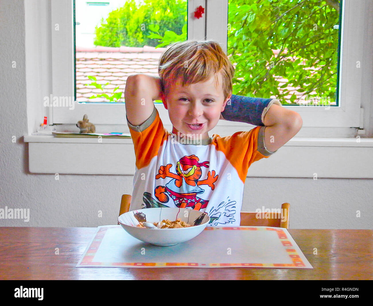 young boy with arm in cast has breakfast at the table Stock Photo