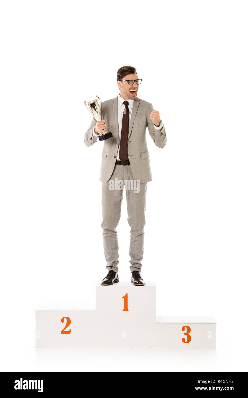 handsome excited businessman with trophy cup standing on winners podium isolated on white Stock Photo