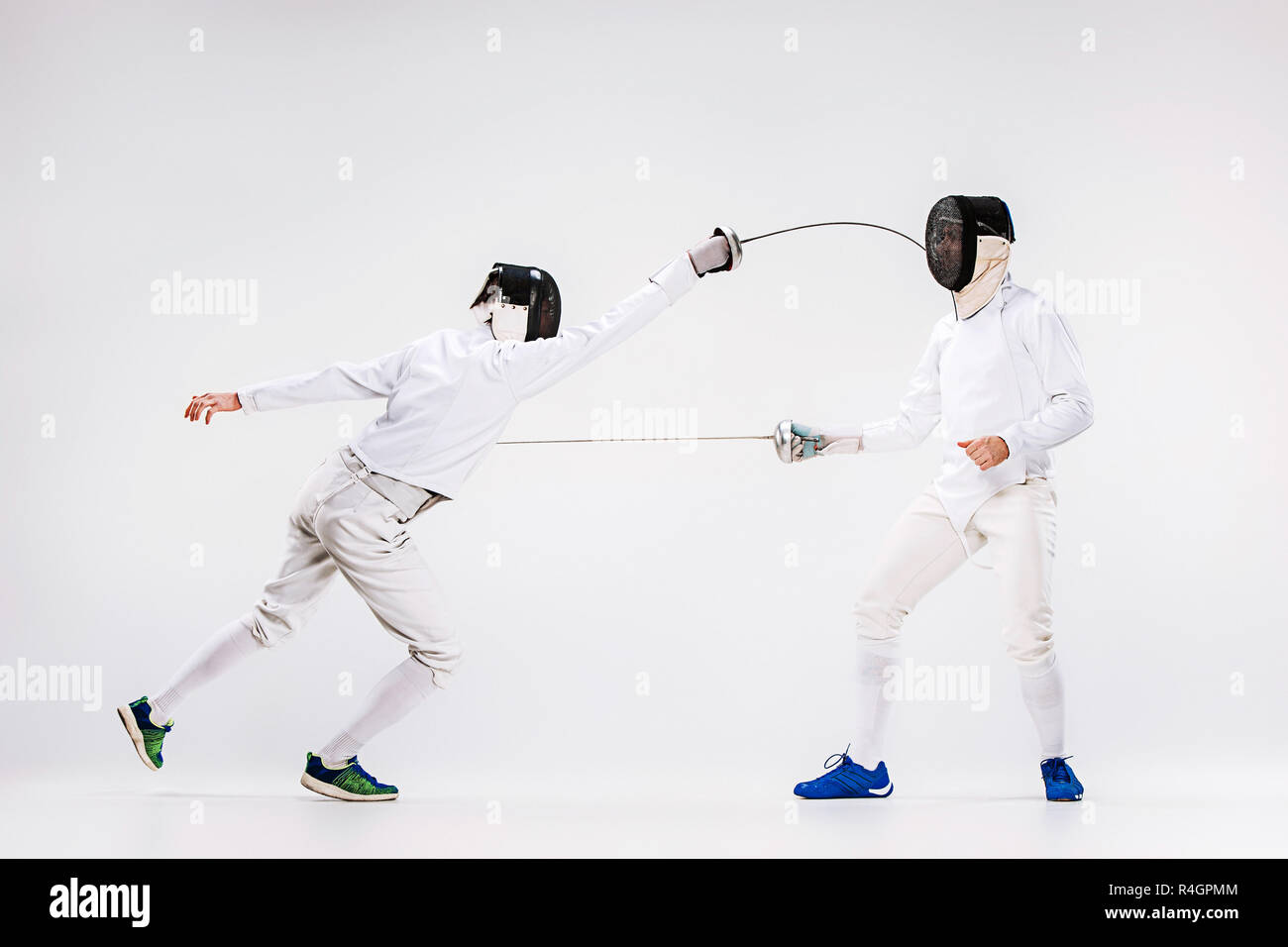 The two men wearing fencing suit practicing with sword against gray