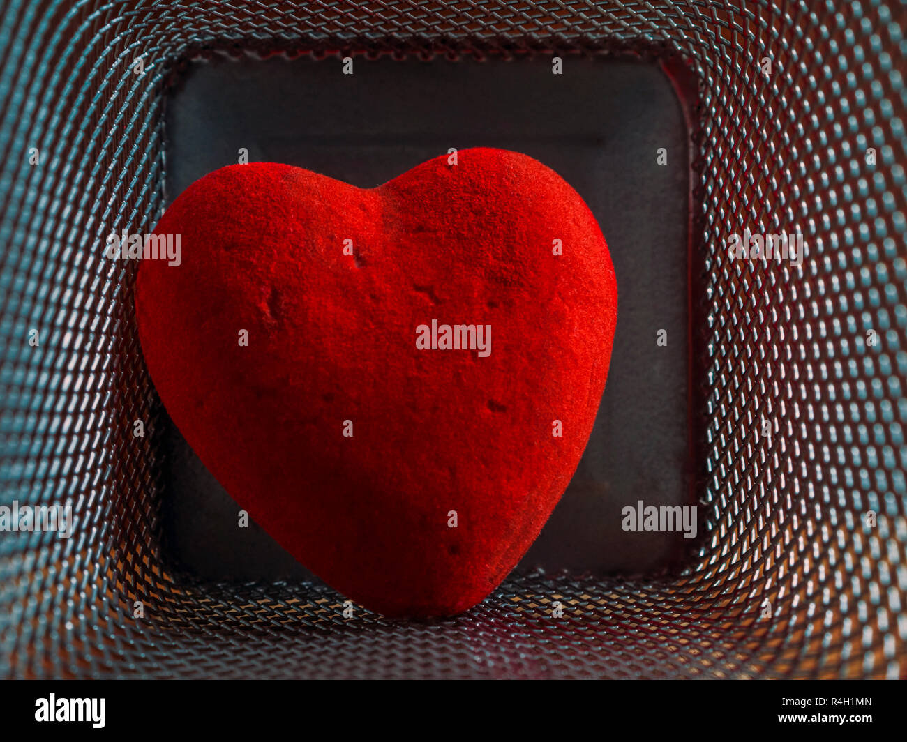 Red Wounded Velvet Heart in a Mesh Cage. Love, Home Violence, Loneliness, Freedom and Heartache Concept. Stock Photo