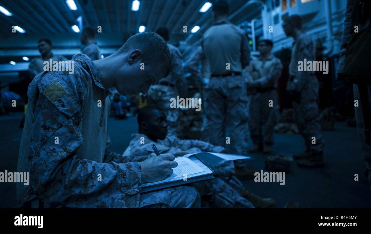 ARABIAN SEA – U.S. Marine Cpl. Andrew Clark, a rifleman with Lima Company, Battalion Landing Team 3/1, 13th Marine Expeditionary Unit (MEU), logs Marines after they return from fast-rope night qualifications aboard the Wasp-class amphibious assault ship USS Essex (LHD 2), Oct. 1, 2018. The Essex is the flagship for the Essex Amphibious Ready Group and, with the embarked 13th MEU, is deployed to the U.S. 5th Fleet area of operations in support of naval operations to ensure maritime stability and security in the Central Region, connecting the Mediterranean and the Pacific through the western Ind Stock Photo